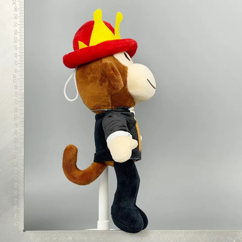 Plush monkey toy wearing a red and yellow hat on a gray background
