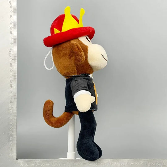 Plush monkey toy wearing a red and yellow hat on a gray background