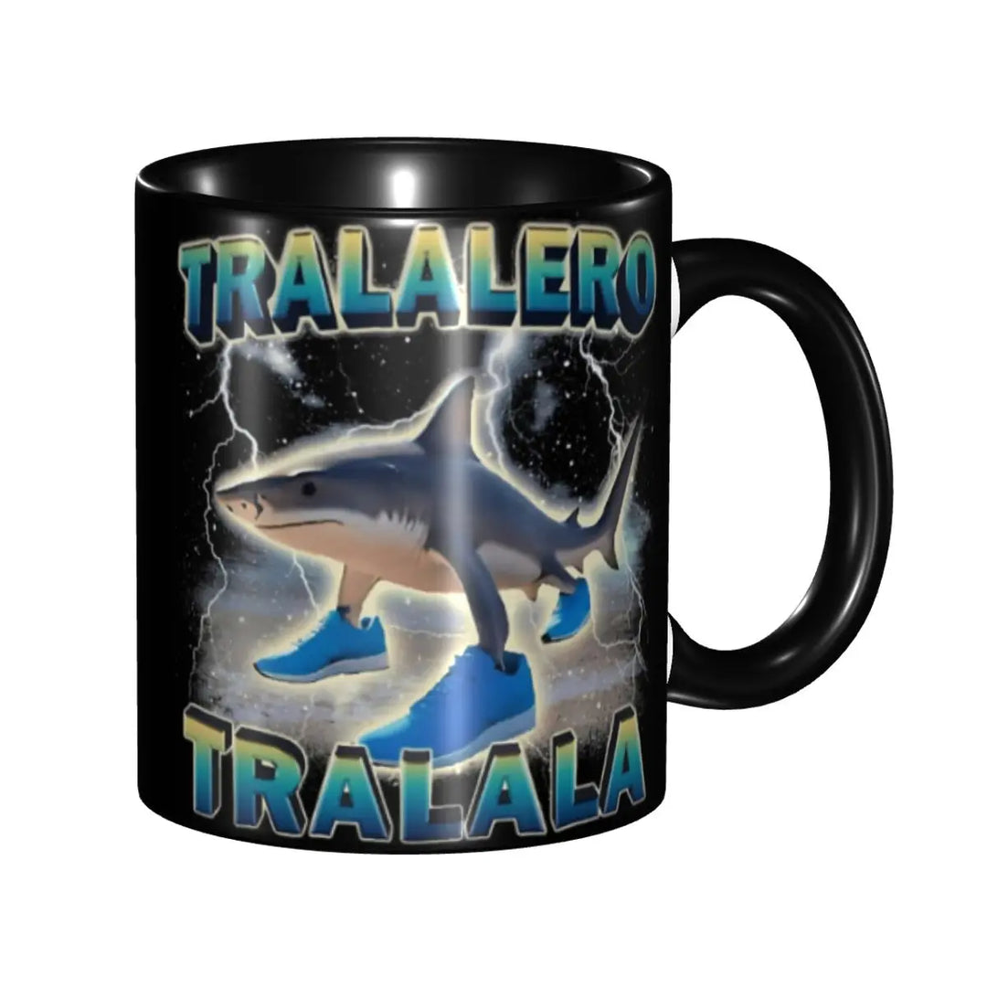 Black ceramic mug with a cartoon shark wearing blue sneakers on a beach and bold white text reading ‘TRALALERO TRALALA,’ shown at a slightly rotated angle.”
