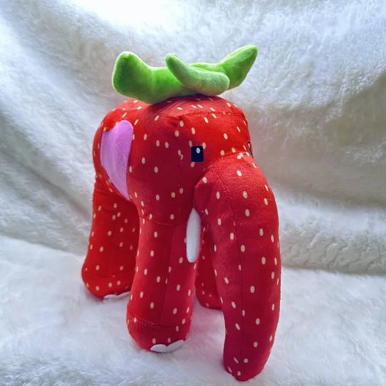 Plush toy shaped like a strawberry elephant on a white blanket