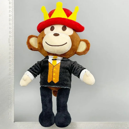 Plush monkey toy with a crown and formal outfit next to a ruler on a gray background