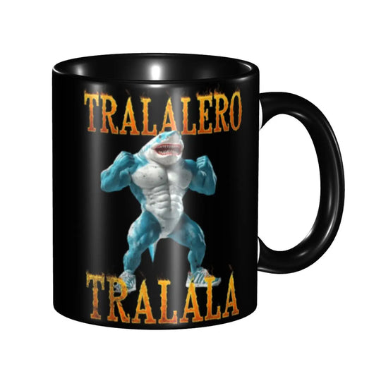 Black ceramic mug with a cartoon human shark wearing blue sneakers on a beach and bold white text reading ‘TRALALERO TRALALA,’ shown from another side angle.