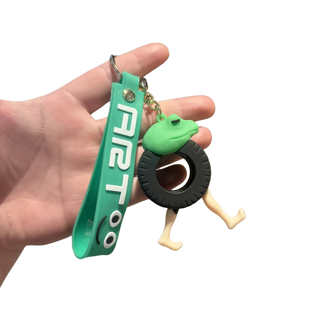 Hand holding a green keychain with a frog design and 'AIRT' branding on a white background